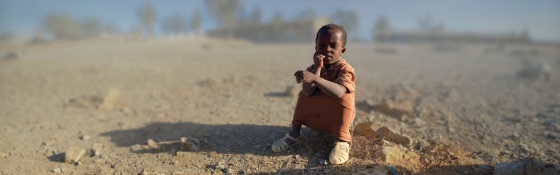 A child sitting on the ground against the backdrop of a dry and barren desert landscape.
